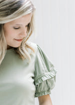 Close up view of short puff sleeve with a ruffle detail on model wearing a sage top. 