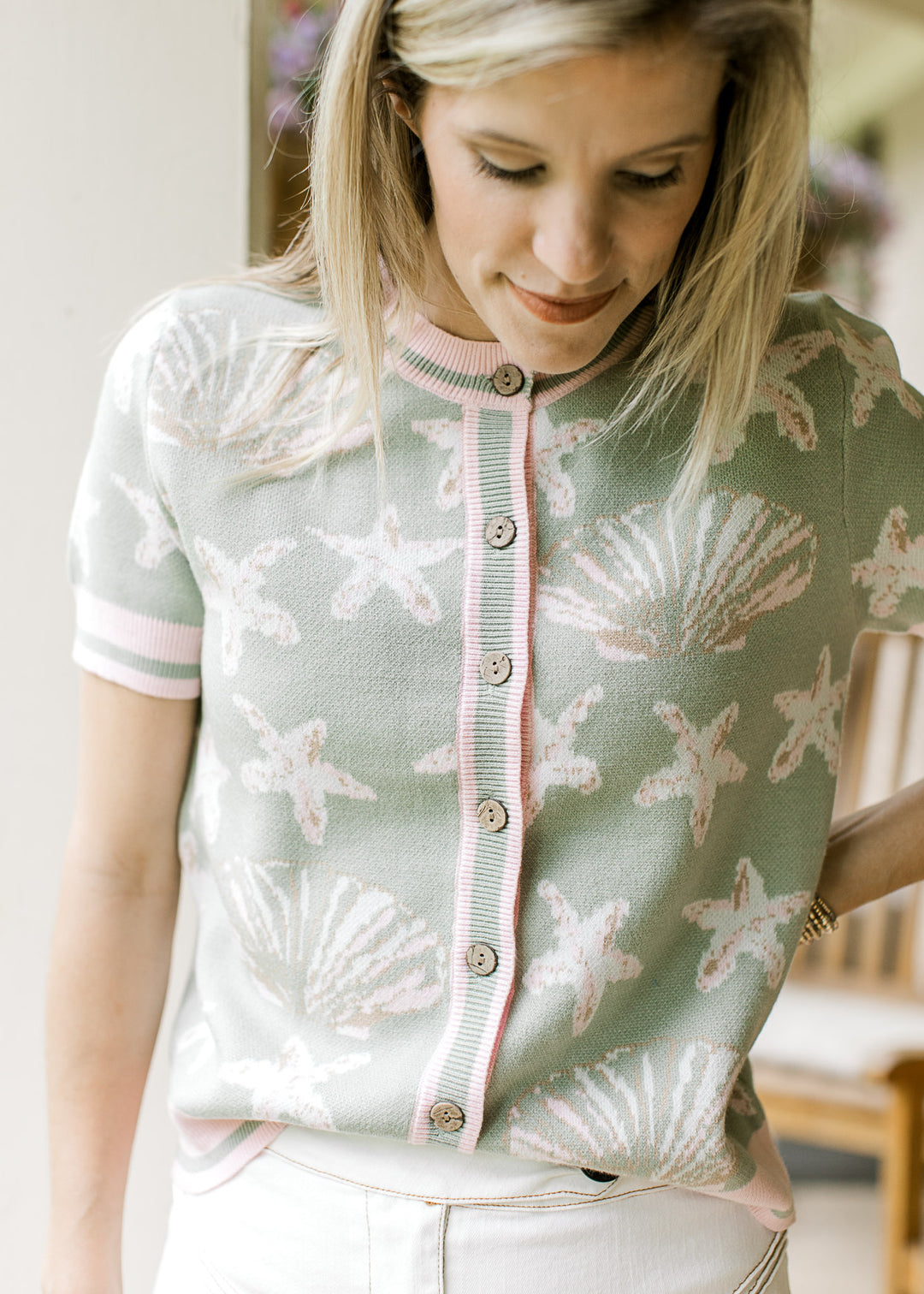 Model wearing a sage short sleeve sweater with shell and starfish motif in white, pink, and taupe.