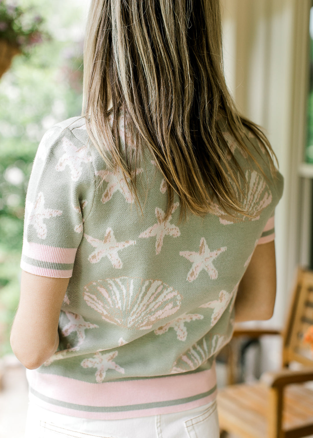 Back view of Model wearing a sage short sleeve sweater with shell and starfish in pink and taupe.