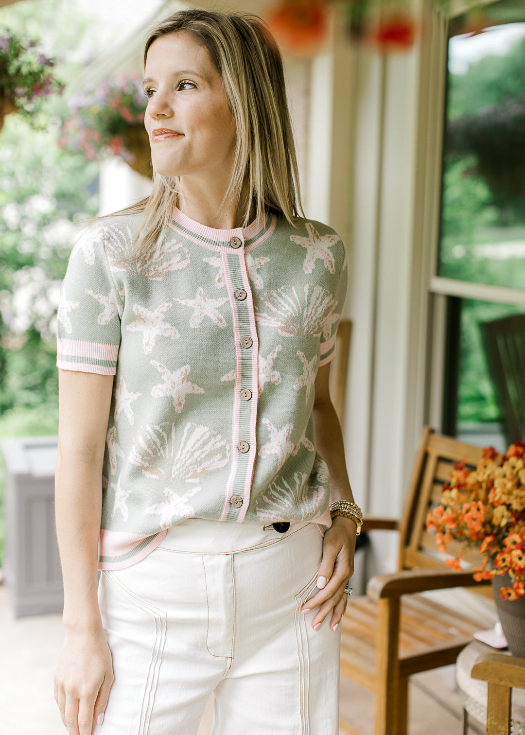 Model wearing a sage button up, short sleeve sweater with shell and starfish motif.