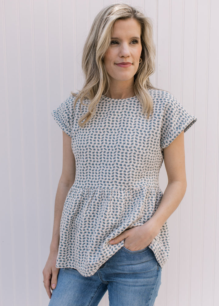 Model wearing a light blue top with tan and cream wavy pattern, round neck and short sleeves.