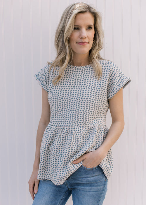 Model wearing a light blue top with tan and cream wavy pattern, round neck and short sleeves.