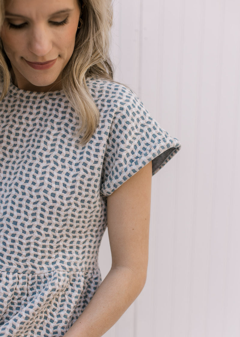 Close up of extended short sleeve on a light blue top with cream and tan wavy pattern. 