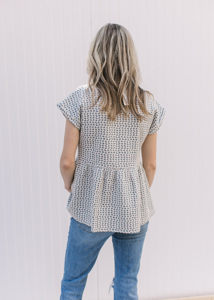Back view of Model wearing a light blue babydoll top with tan and cream pattern and extended sleeves