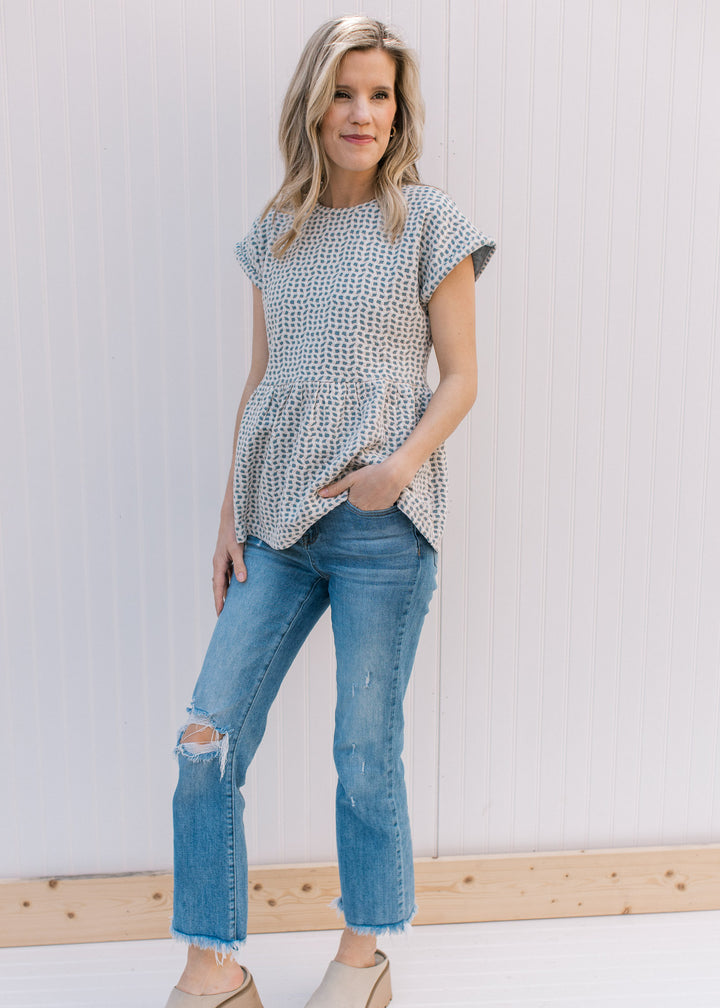 Model wearing jeans with a light blue babydoll top with tan and cream wavy pattern. 