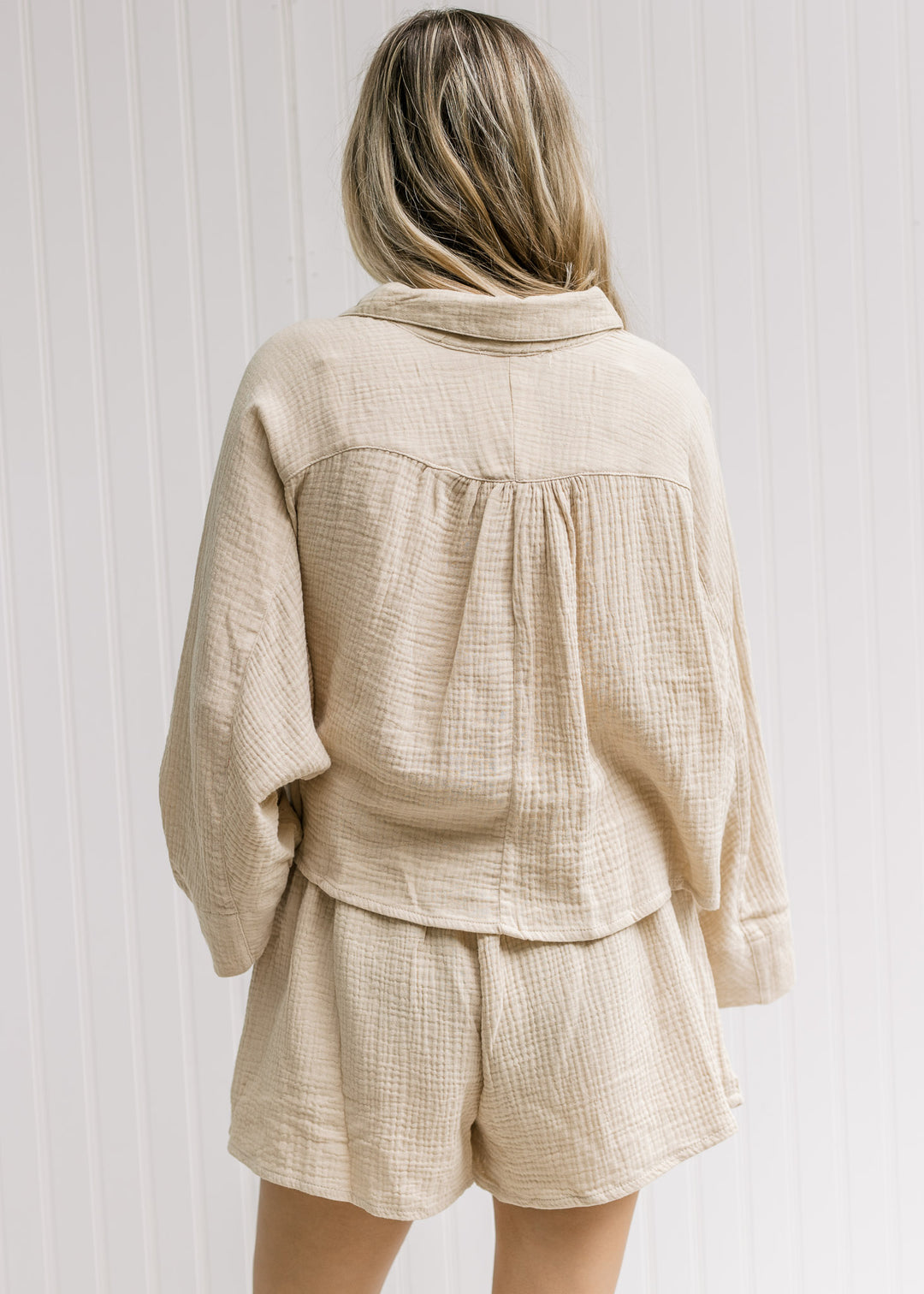 Back of model wearing a sand short set, top has dolmain sleeves and button closure.