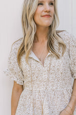 Close up of v-neck with a tie on a white time with sand flowers and a peplum fit. 