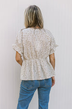 Back view of Model wearing a white top with sand flowers a v-neck with tie detail and a peplum cut.