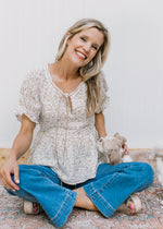 Model with a puppy wearing a white top with sand flowers a v-neck with tie detail and a peplum cut.