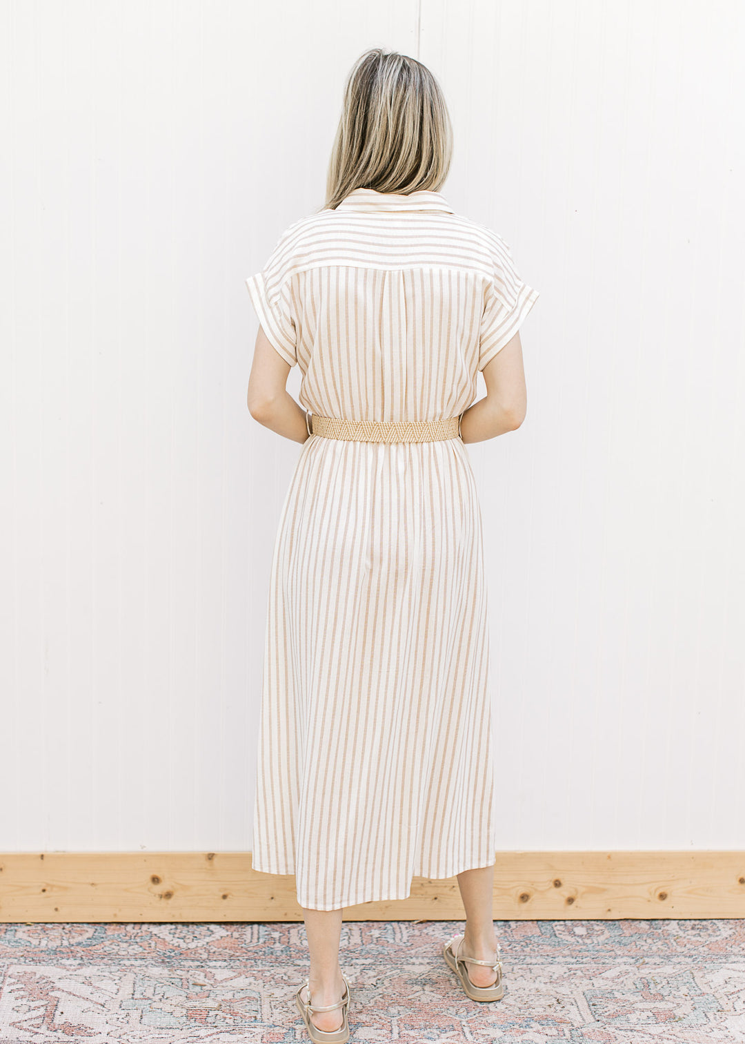 Back view of Model wearing a cream midi with sand stripes, collar and elastic waist with belt.