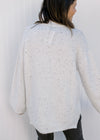 Back view of Model wearing an off white long sleeves sweater with black flecks and a mock neck. 