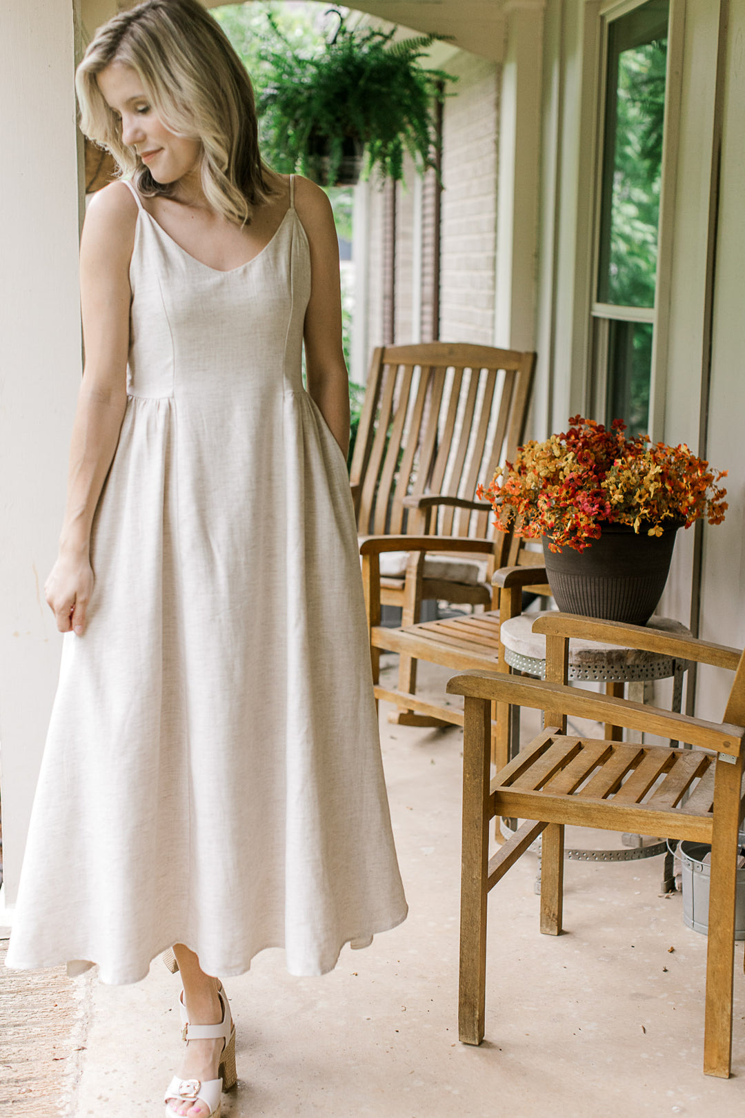 Model wearing a sand-colored midi with adjustable spaghetti straps, v-neck and side pockets.
