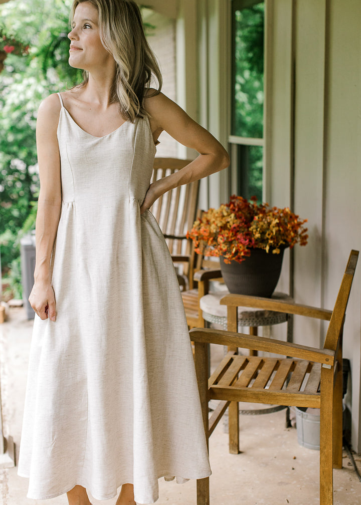 Model wearing a sand-colored midi with adjustable spaghetti straps, v-neck and a smocked back panel.