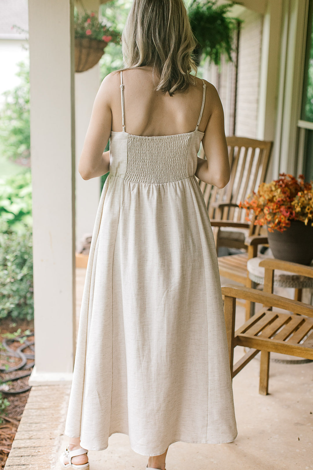 Back view of Model in a sand-colored midi with adjustable spaghetti straps, and a smocked back.