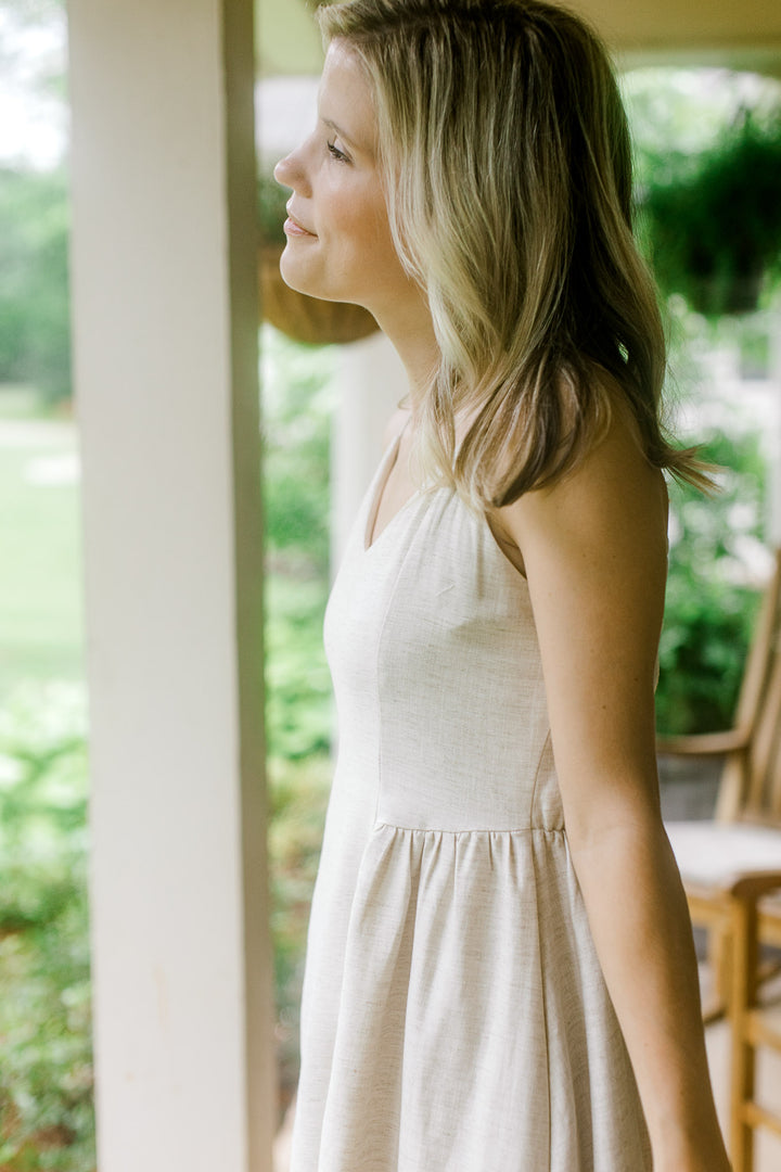 Side view of model wearing a sand midi with adjustable spaghetti straps, v-neck and a smocked back.