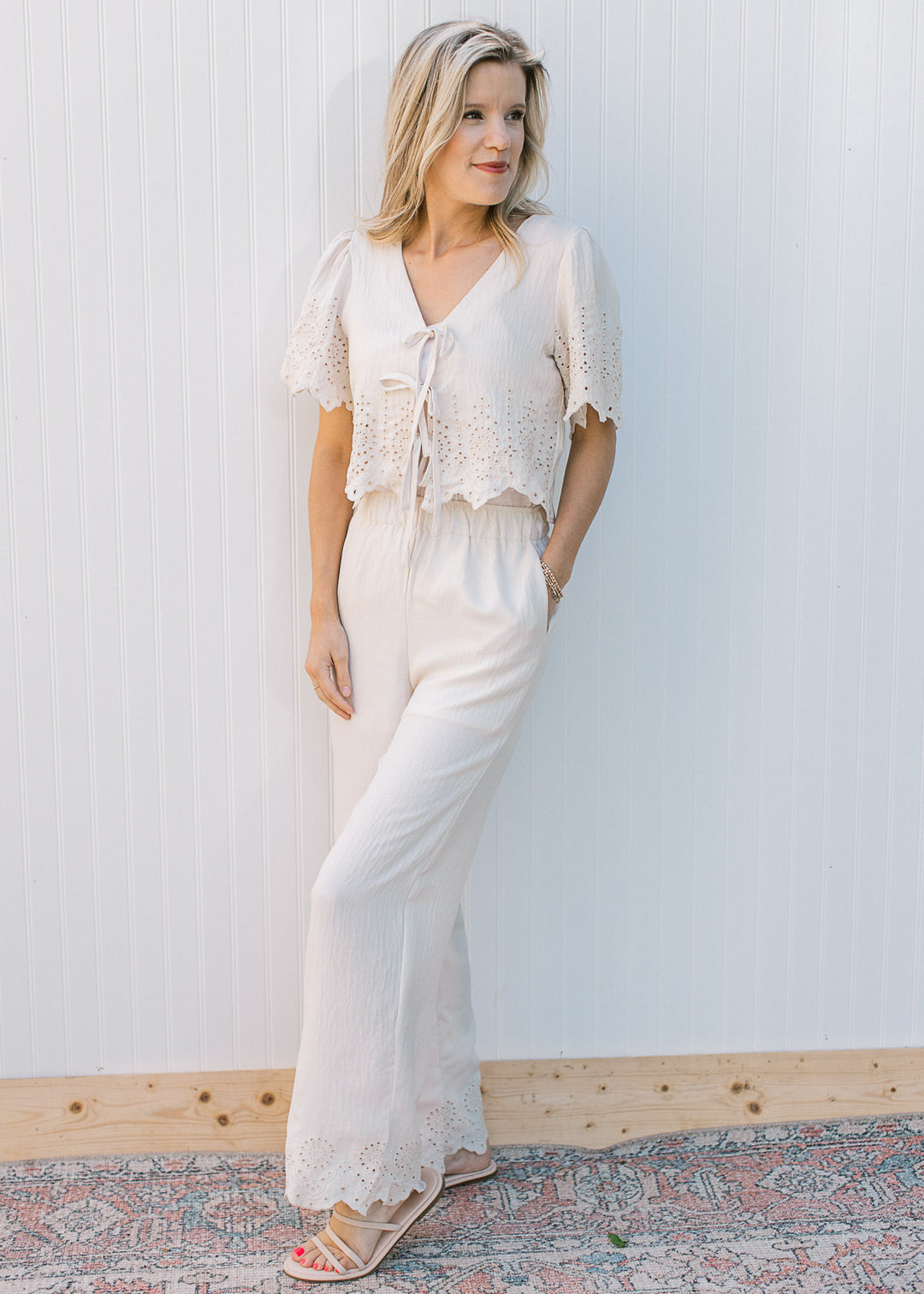 Model wearing a cream set with scalloping and eyelet details at both pant and top hemlines. 