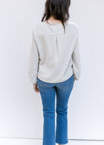 Back view of Model wearing a cream top with bubble long sleeves and a side button detail.