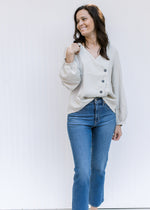 Model wearing jeans with a cream polyester top with bubble long sleeves and a side button detail.