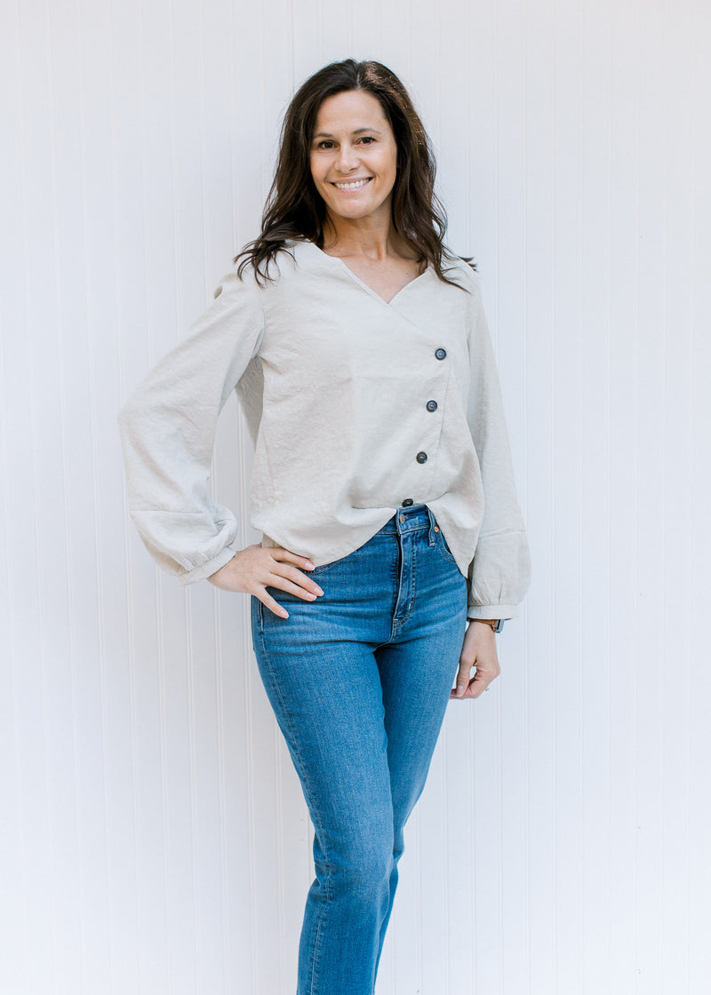Model wearing jeans a cream top with bubble long sleeves and a side button detail.