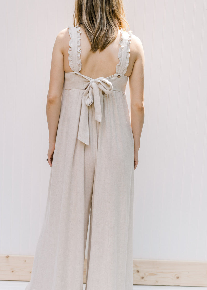 Back view of model wearing a sand colored wide leg jumpsuit with a tie in back. 