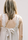 Close up view of tie on back of a sand colored jumpsuit with adjustable button straps. 