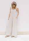 Model wearing a sand colored jumpsuit with adjustable button straps and wide legs. 