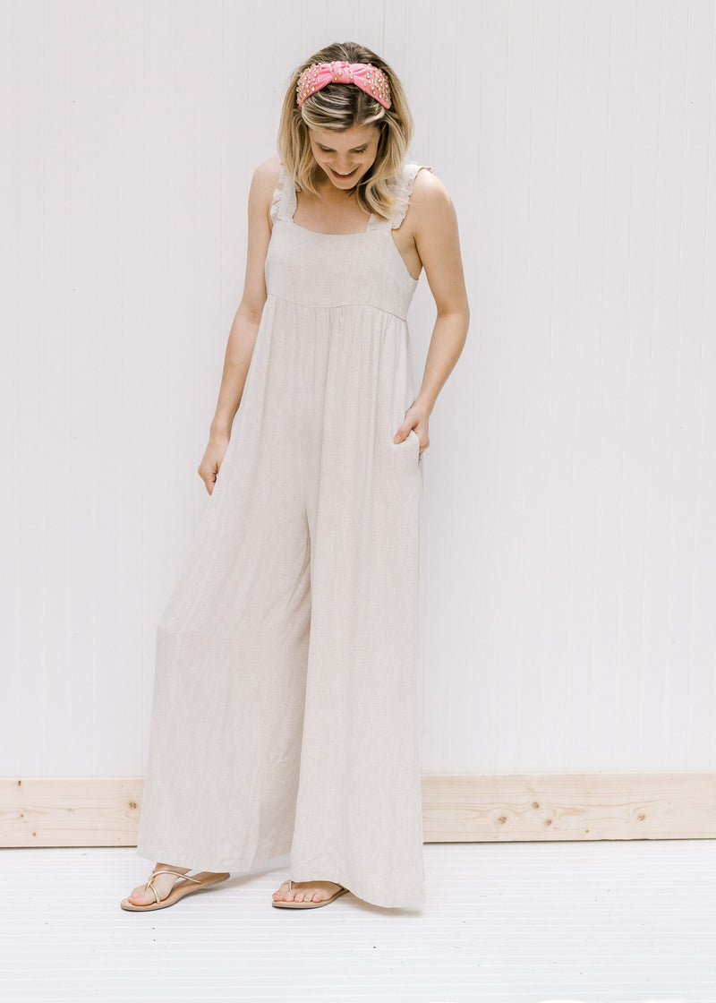 Model wearing a sand colored jumpsuit with adjustable button straps and wide legs. 