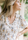 Close up of smocked bodice, v-neck with a ruffle and sheer bubble sleeves on a hite floral dress.