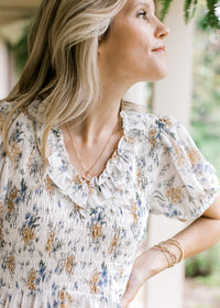 Close up of smocked bodice, v-neck with a ruffle and sheer bubble sleeves on a hite floral dress.
