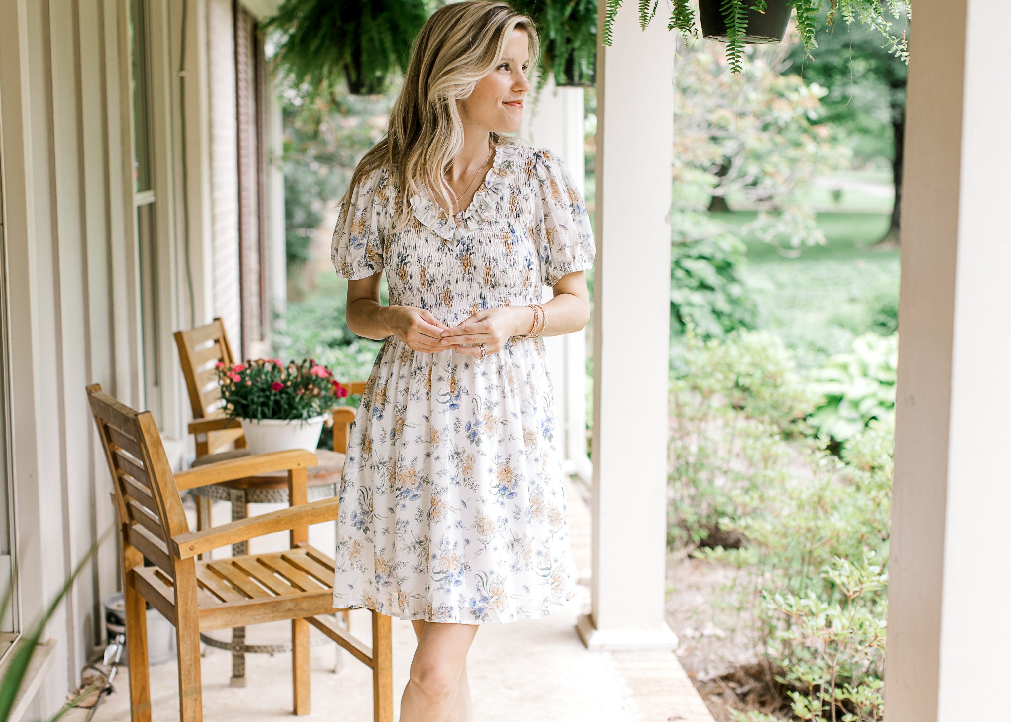 Model wearing a white short sleeve dress with yellow and blue floral and a smocked bodice. 