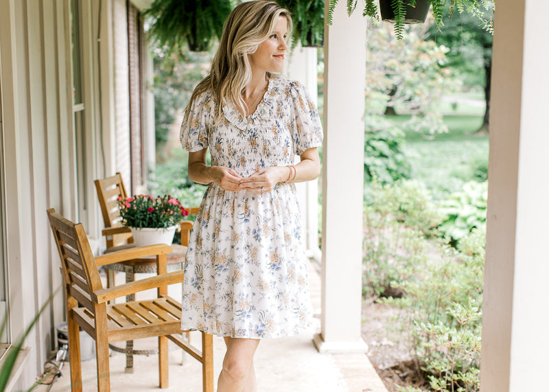 Model wearing a white short sleeve dress with yellow and blue floral and a smocked bodice. 