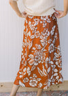 Back view of Model wearing a burnt orange midi with white flowers and an elastic waist with a tie. 