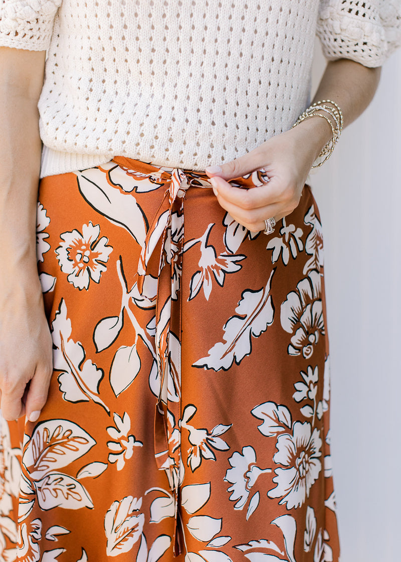 Close up of elastic waist with a tie on an burnt orange midi with white flowers. 