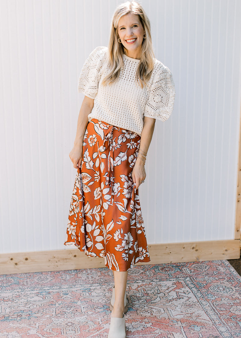 Model wearing a burnt orange midi with white flowers and an elastic waist with a tie. 