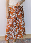 Model wearing a cream top with a burnt orange midi with white flowers and an elastic waist.