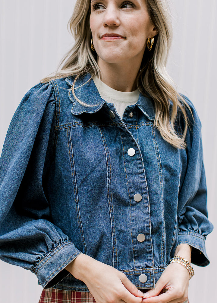 Model wearing a medium/dark wash denim button up jacket with scalloped flap collar. 