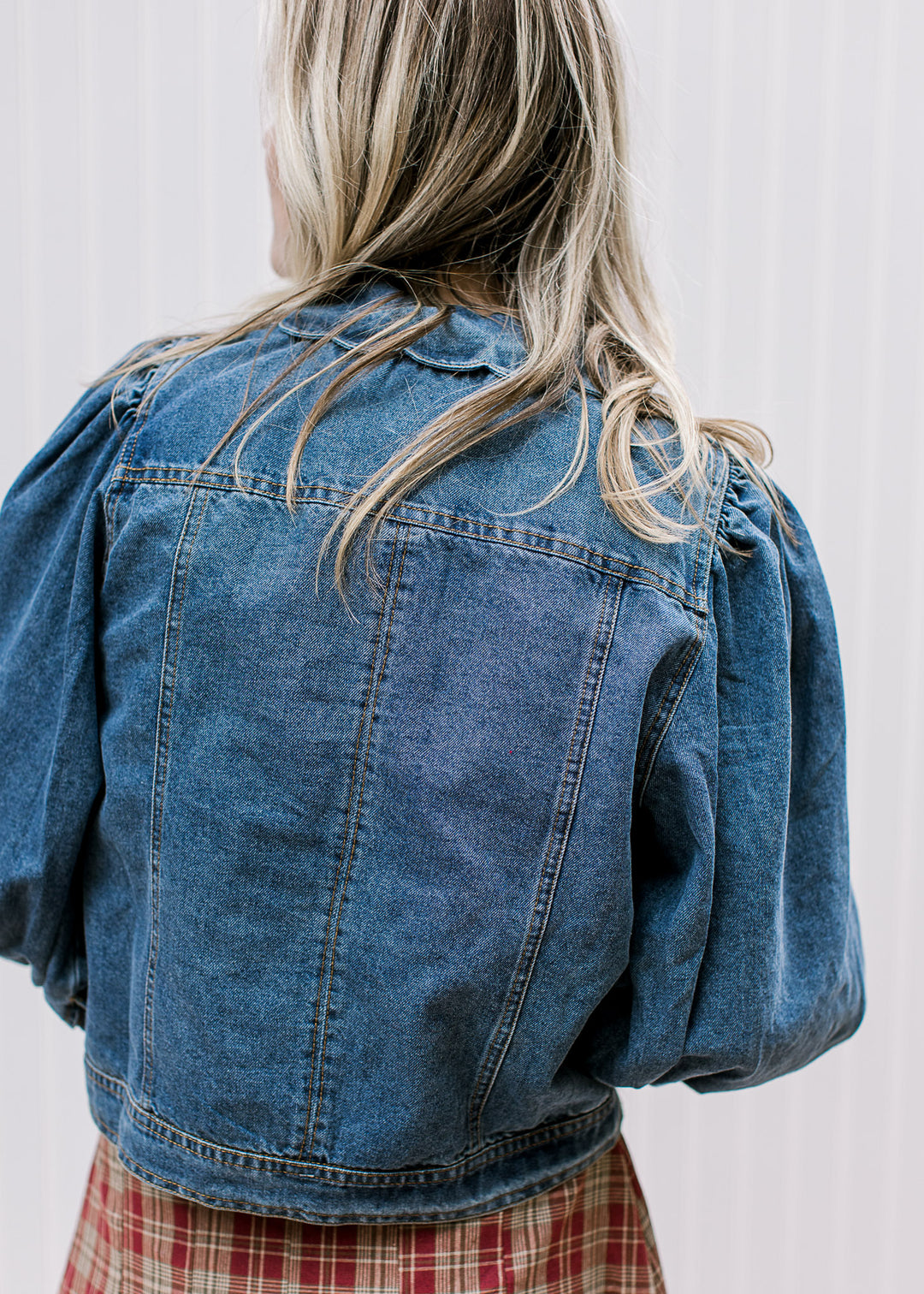 Back view of Model wearing a medium/dark wash denim jacket with scalloped flap collar. 