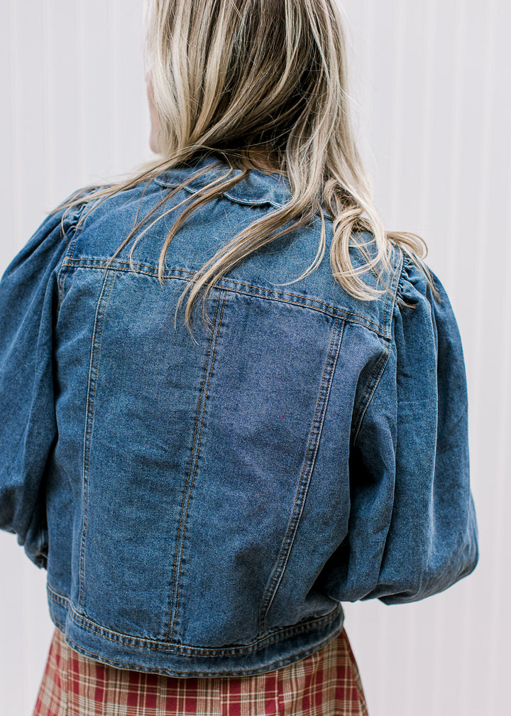 Back view of Model wearing a medium/dark wash denim jacket with scalloped flap collar. 