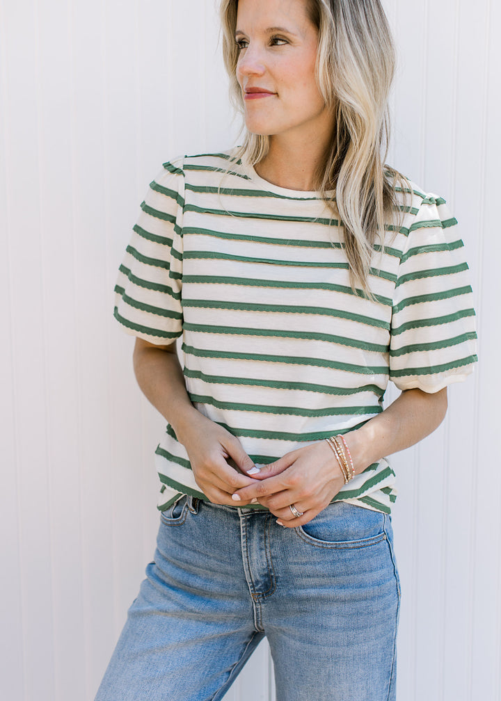 Model wearing a cream top with green scalloped stripes, short bubble sleeves and a round neck.
