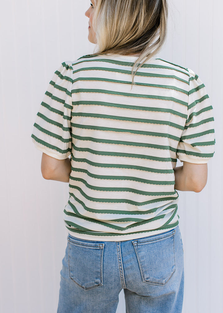 Back view of Model wearing a cream top with green scalloped stripes, short sleeves and round neck.
