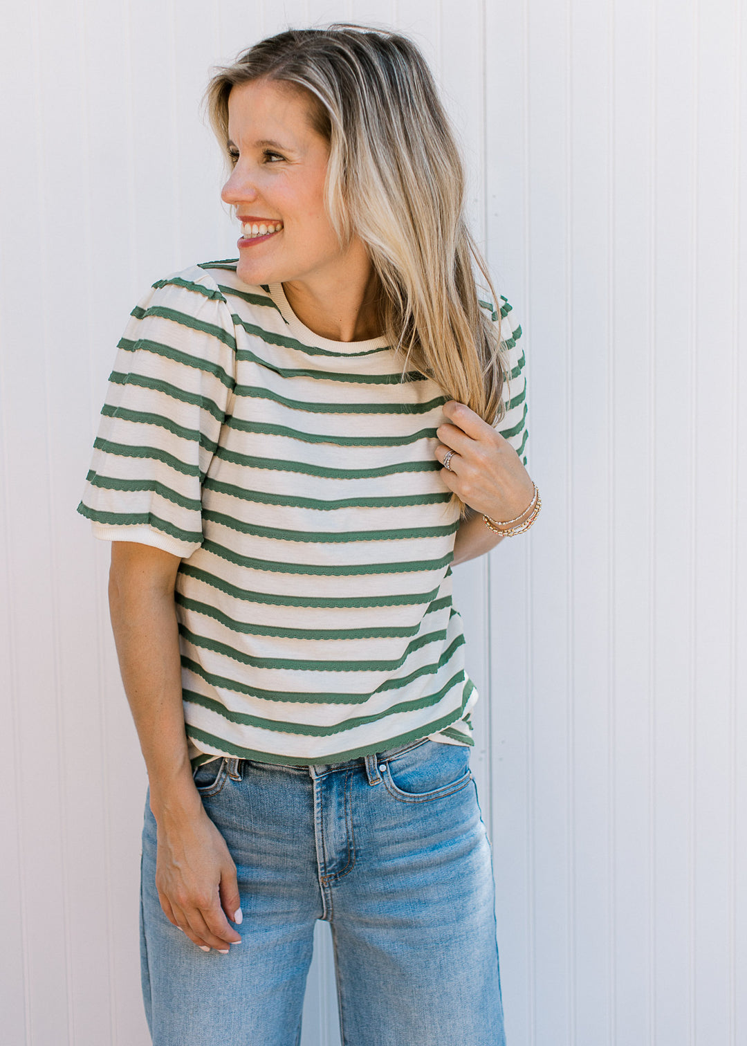 Model wearing jeans and a cream top with green scalloped stripes, short sleeves and a round neck.
