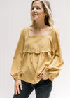 Model wearing a mustard square neck top with a scalloped detail at neck and breast and long sleeves.