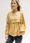 Model wearing a mustard top with scalloped detail at neck and breast, square neck and long sleeves.
