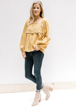 Model wearing jeans, booties and a mustard square neck top with a scalloped detail and long sleeves.