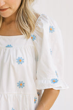Close up view of bubble short sleeves and a square neck on a white top with blue daisies. 
