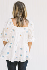 Back view of Model wearing a white top with blue daisies, a square neckline and a babydoll fit.