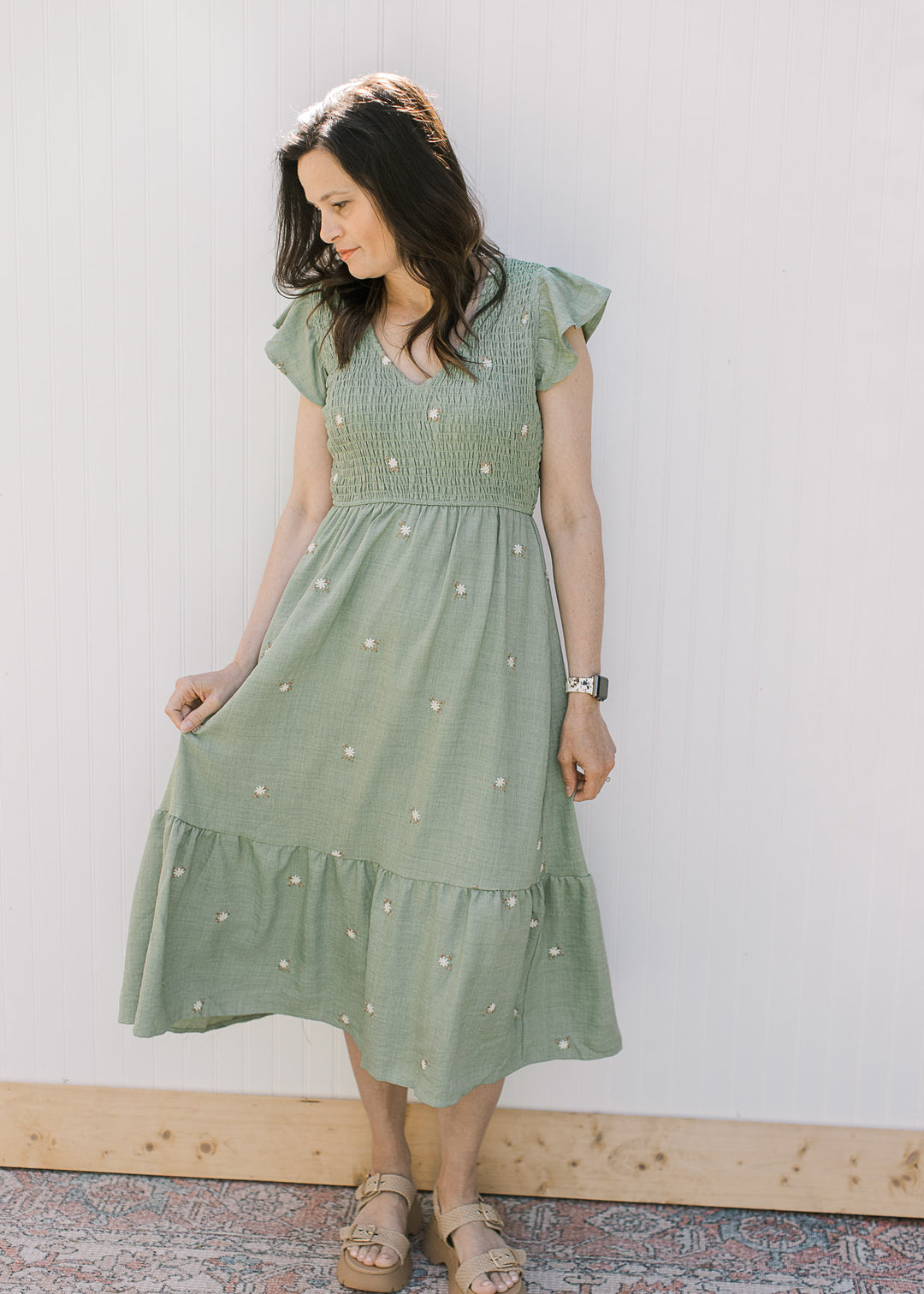 Model is wearing a sage green midi with cream embroidered flowers, a smocked bodice and v-neck.