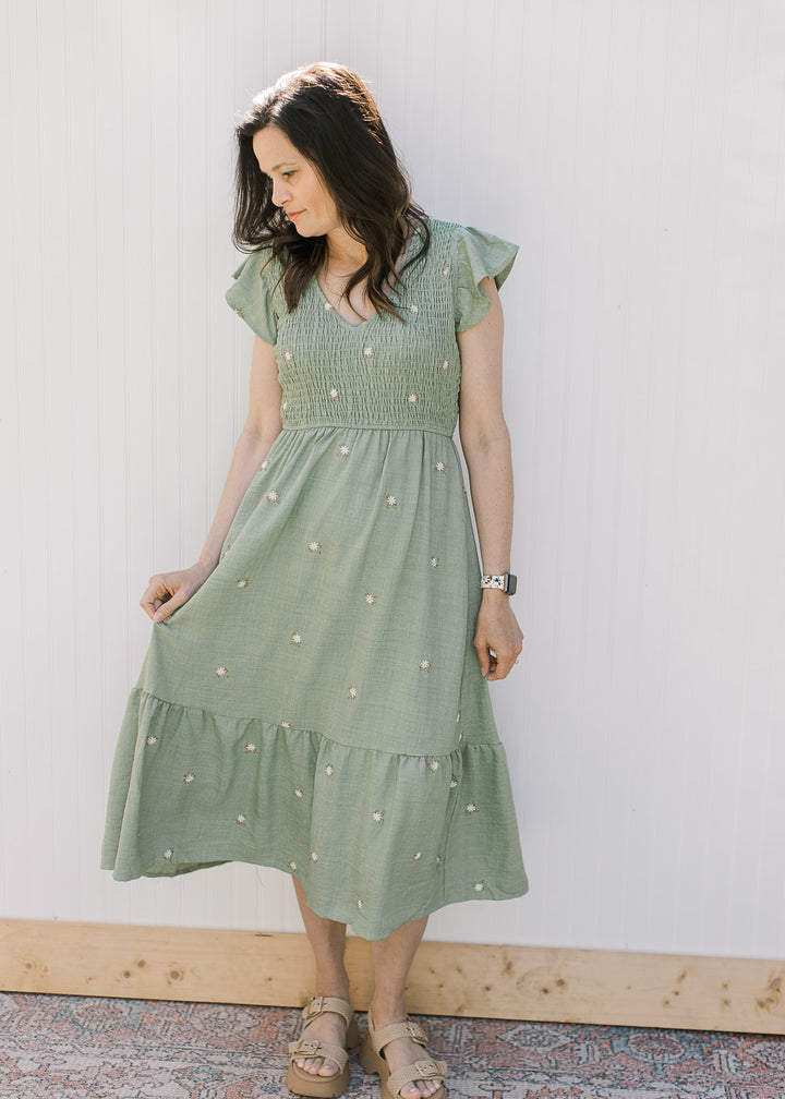 Model is wearing a sage green midi with cream embroidered flowers, a smocked bodice and v-neck.