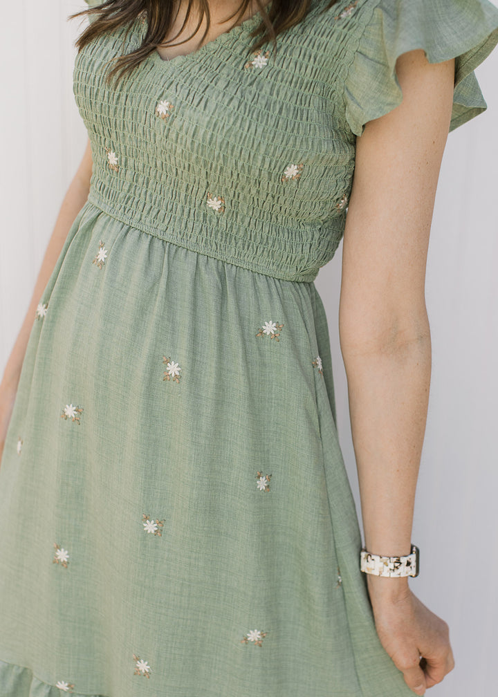 Close up of smocked bodice and cream embroidered flowers on a sage midi with flutter sleeves. 