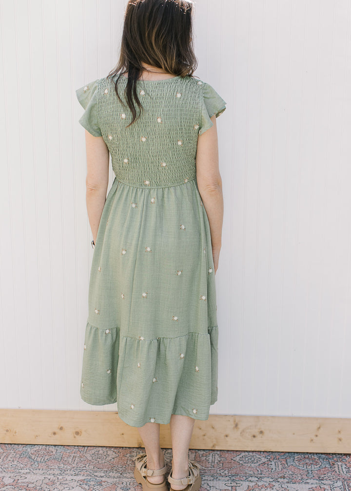 Back view of Model is wearing a sage green midi with cream flowers, and a smocked bodice. 